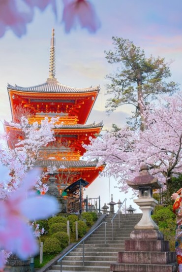 A young Japanese woman in a traditional kimono in front of the Kiyomizu-dera Temple in Kyoto embodies elegance and Japanese culture, amid ancient architecture and scenic views.