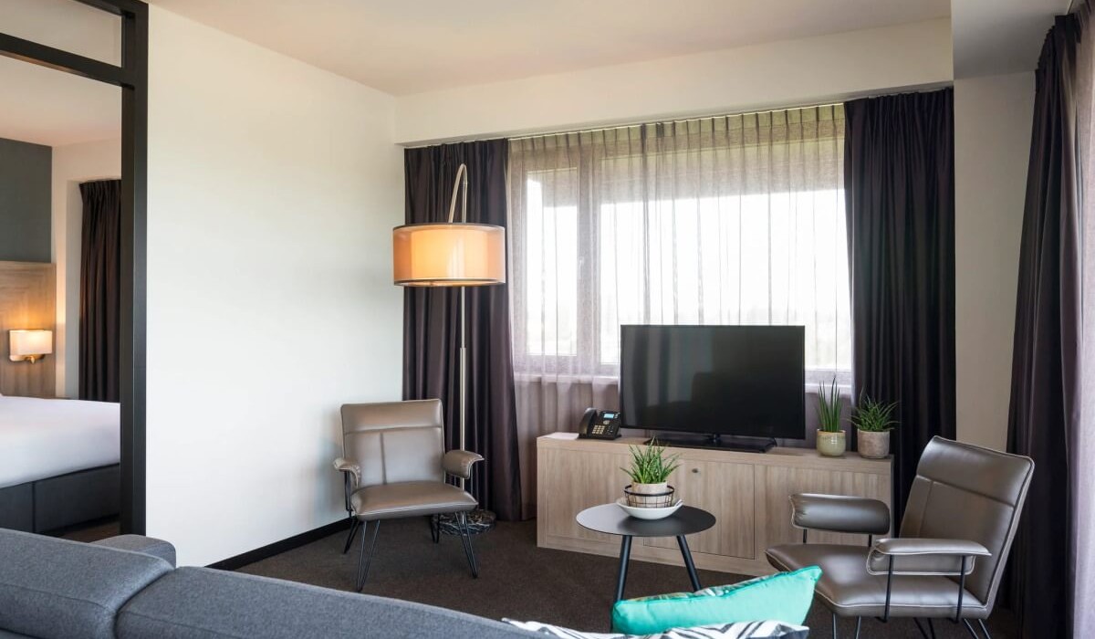 Adagio Amsterdam City South - The living room of the Junior Apartment features a TV corner with satellite channels, a comfortable sofa, and two armchairs, creating a cozy space perfect for relaxing.