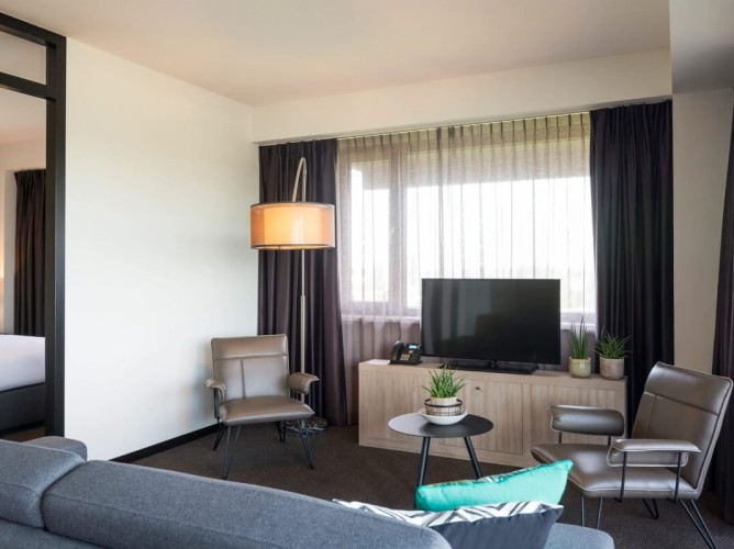 Adagio Amsterdam City South - The living room of the Junior Apartment features a TV corner with satellite channels, a comfortable sofa, and two armchairs, creating a cozy space perfect for relaxing.