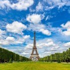 The green expanse of the Champ de Mars unfolds like a vast lawn, crossed by tree-lined paths and colorful blooms, while the Eiffel Tower elegantly dominates the background.