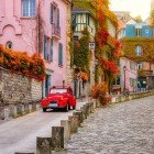 A cozy street in Montmartre, with autumn leaves carpeting the cobbled lanes. A classic red Diane car stands out against the picturesque backdrop of the Parisian district.