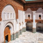 The walls of the Ben Youssef Madrasa courtyard feature multicolored zellige tiles at the bottom and stucco carvings above, with handcrafted carved wooden windows.