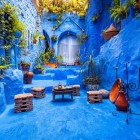 A typical courtyard in the blue medina of Chefchaouen, with terracotta pots, a small table, and rustic chairs, conveys warmth and authenticity in Moroccan tradition.