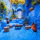 A typical courtyard in the blue medina of Chefchaouen, with terracotta pots, a small table, and rustic chairs, conveys warmth and authenticity in Moroccan tradition.