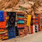 In the Tinghir souq, Moroccan rugs with vibrant colors and traditional patterns decorate the shops, expressing authentic local craftsmanship.