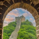 View of the Great Wall of China through an arch, among towers and vegetation, showcasing ancient Chinese military architecture in a breathtaking landscape.