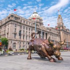 Bronze bull statue on Shanghai’s Bund, a symbol of strength and prosperity, set between the riverside and the city skyline.