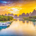 Sunset cruise on the Li River in Guilin, among karst mountains illuminated by golden light and calm waters reflecting the clear sky.