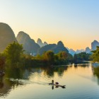 Yangshuo at sunset, with the karst mountains turning shades of orange and red, and traditional villages bathed in golden light.