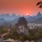Fubo Hill in Guilin at sunset towers above traditional houses, with its karst formations illuminated by the golden light of the setting sun.