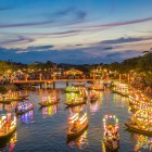 Boats illuminated by lanterns sail on Hoi An’s river, amidst reflections on the water and the romantic atmosphere of the historic Vietnamese town.