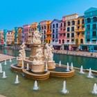 In the center of the square, the fountain sparkles among the bright colors of the day, surrounded by Italian-style buildings reflected in the canal.