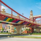A colorful bridge in Hanoi with European architecture and vibrant rainbow tones stands out among modern buildings and blue skies, creating a bright and lively scene.