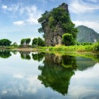 A karst tower rises above the calm waters of the Ngo Dong River in Tam Cốc, with perfect reflections and breathtaking natural landscapes.