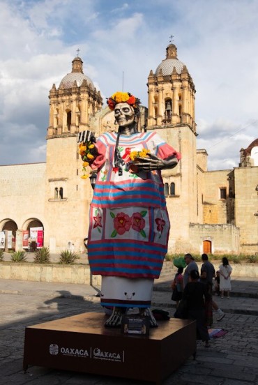 Colorful Catrina in front of Santo Domingo Church in Oaxaca: the Día de los Muertos figure stands out against the baroque architecture as visitors walk through the square.