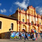 San Cristóbal de la Casas Cathedral, with its vibrant yellow-red baroque façade and colorful murals below, stands out in the square, showcasing the unique colonial charm of Chiapas.