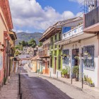 Colonial street in San Cristóbal, lined with colorful houses, flowered balconies and terracotta roofs, set against the Chiapas mountains. An authentic, charming corner.
