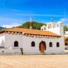 The Church of San Lorenzo in Zinacantán, Chiapas, captivates with its white façade and colorful details, serving as the spiritual center of the Tzotzil community and a symbol of Indigenous traditions.