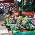 A Tzotzil woman and child at the San Cristóbal market display fresh fruit on green and light-blue cloths, creating an authentic scene filled with color, tradition and Indigenous daily life.