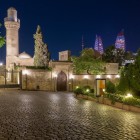 The Shirvanshahs Palace at night in Baku captivates with illuminated domes and minarets, set between ancient walls and the modern skyline in the background.