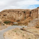 The Diri Baba Mausoleum in Azerbaijan, set into the rock, overlooks an arid landscape with a historic staircase, scenic road and evocative hills.