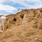 The Diri Baba Mausoleum, set into the rock in Azerbaijan, features a white dome, stone arches and an arid landscape with striking rocky hills.