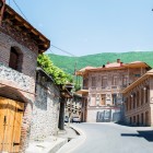 Typical historic houses of Sheki, Azerbaijan, with stone and brick façades, wooden balconies and traditional roofs, set among the green hills of the High Caucasus.