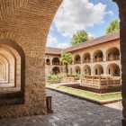 Stone porticoes and arches open onto the courtyard of the Sheki Caravanserai, with a central garden and historic atmosphere in the heart of the Caucasus.