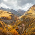 Spectacular autumn landscape along the Georgian Military Road: golden valleys, deep canyons and Caucasus peaks wrapped in clouds, amid silence and wild nature.