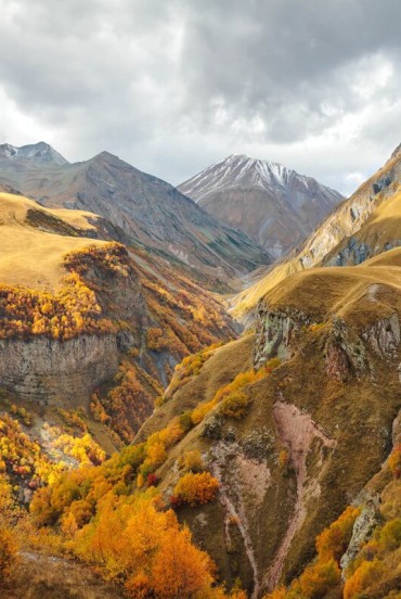 Spectacular autumn landscape along the Georgian Military Road: golden valleys, deep canyons and Caucasus peaks wrapped in clouds, amid silence and wild nature.