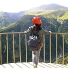 A traveler admires the Devil’s Valley from the Friendship Monument in Gudauri: green canyons and Caucasus mountains unfold in a breathtaking panorama.