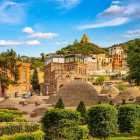 In the heart of Tbilisi, the domes of the sulfur baths rise among manicured gardens and colorful houses, with the hill and a church overlooking the view.