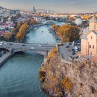 The Metekhi Church rises on a rocky cliff above the Kura River, framing bridges and Tbilisi’s skyline in a striking urban setting.