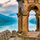Panoramic view from Ananuri Fortress over Lake Zhinvali: ancient stone arches frame the turquoise waters and the Caucasus mountains, creating a striking landscape.