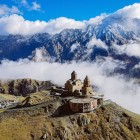 The Gergeti Trinity Church rises among the clouds at the foot of Mount Kazbek, overlooking the landscapes of the Greater Caucasus, surrounded by majestic peaks and alpine silence.