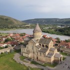 Aerial view of the majestic Svetitskhoveli Cathedral in Mtskheta, an ancient religious center of Georgia, with the Mtkvari River and green hills surrounding the city.