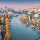 Aerial view of Tbilisi, with the Mtkvari (Kura) River crossing the city, the Peace Bridge and riverside parks blending historic and modern architecture.