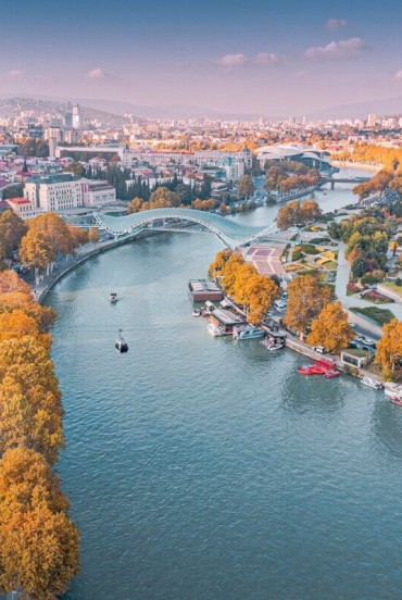 Aerial view of Tbilisi, with the Mtkvari (Kura) River crossing the city, the Peace Bridge and riverside parks blending historic and modern architecture.