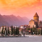 Svetitskhoveli Cathedral in Mtskheta at sunset, bathed in warm golden light, with the Caucasus mountains in the background and the charming atmosphere of Georgia’s ancient capital.