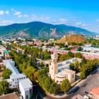 Aerial view of Gori, Georgia, with the historic Gori Fortress rising above the city from the hill, surrounded by modern districts and the Caucasus mountains.