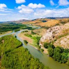 Aerial view of the rock-hewn city of Uplistsikhe, an ancient settlement carved into the rock overlooking the Mtkvari River, surrounded by hills and stunning Georgian landscapes.