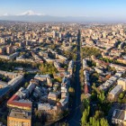 Aerial view of Yerevan with lively Mashtots Avenue crossing the city between buildings, tree-lined streets and historic districts, with majestic Mount Ararat on the horizon.