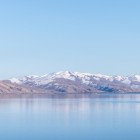 View of Lake Sevan, Armenia: calm, crystal-clear waters reflect snow-capped mountains, creating a stunning alpine landscape and one of the country’s most iconic natural sights.