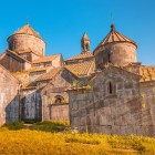 View of Haghpat Monastery in Armenia, with stone churches and conical domes lit by golden light, featuring medieval details and a suggestive atmosphere.
