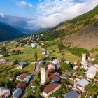 Aerial view of Mestia, in the heart of Svaneti, with medieval stone towers among green meadows and alpine landscapes, dominated by the majestic Caucasus peaks.