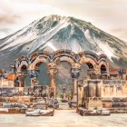 Ancient ruins of the Zvartnots Cathedral in Armenia, with elegant carved stone arches set against the majestic snow-capped Mount Ararat.