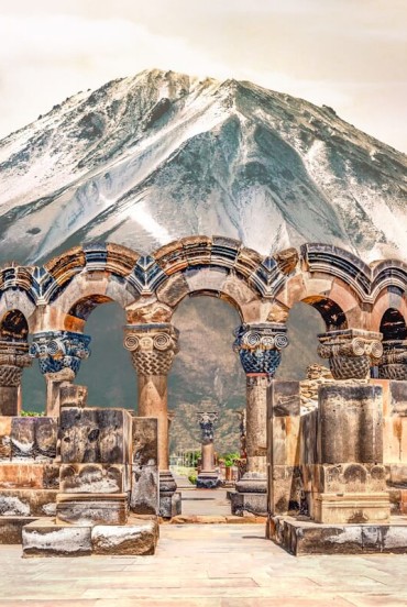 Ancient ruins of the Zvartnots Cathedral in Armenia, with elegant carved stone arches set against the majestic snow-capped Mount Ararat.