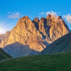 The majestic peaks of Mount Chaukhebi glow in golden light at sunset, dominating alpine valleys and spectacular landscapes in Kazbegi National Park.