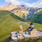 The Gergeti Trinity Church stands above the hills of Stepantsminda, overlooking the valleys of Kazbegi with Mount Kazbek rising in the background.