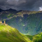 Gergeti Trinity Church overlooks the hills of Kazbegi, set between green meadows and the towering Caucasus peaks rising across the horizon.